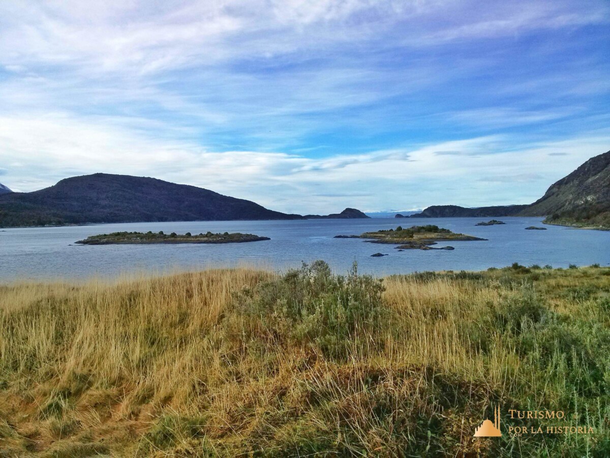 Primer plano de pastizales, de fondo las aguas de la bahía con islotes de pasto y a los costados montañas bajas. Ushuaia